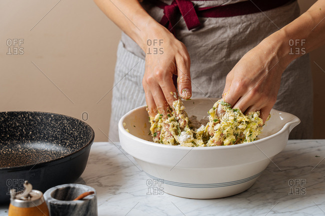 Woman mixing ingredients for zucchini fritters together in a bowl by hand