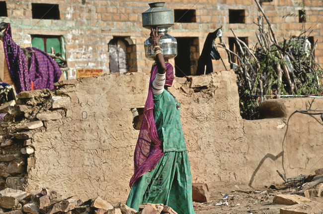 India, Rajasthan, Jaisalmer - August 16, 2011: Rajasthani carrying water jars in the head in a Thar Desert village