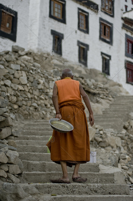 Old monk carrying a tray walking up the monastery ladder