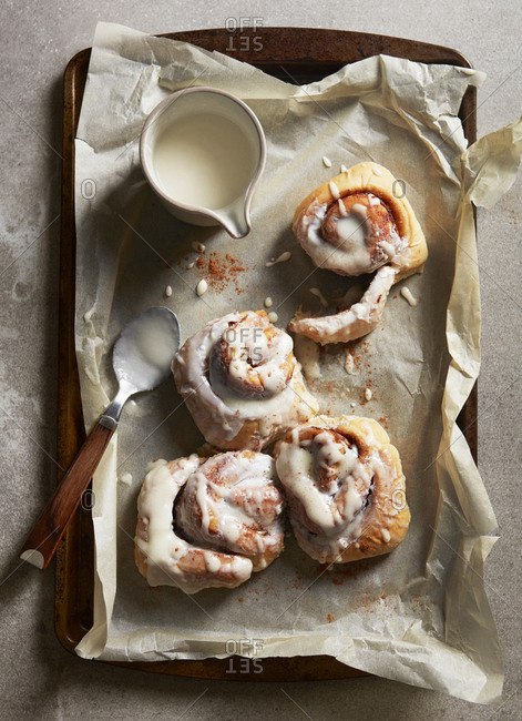 Frosting cinnamon rolls on tray with spoon