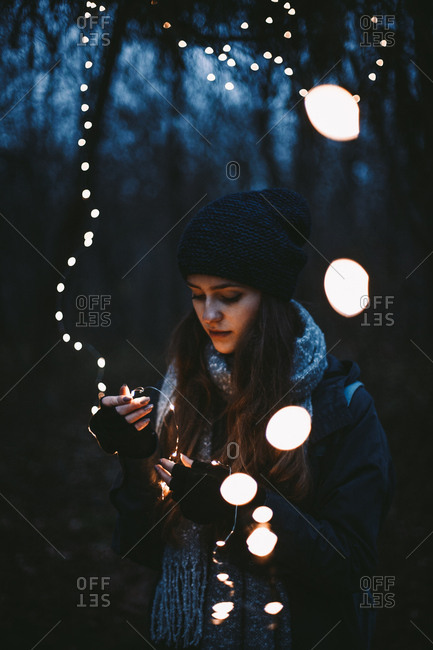 Young hipster woman holding Christmas lights while standing in park