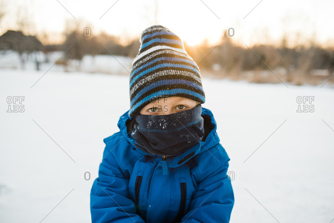 Young boy looking at camera with blue scarf and winter hat.