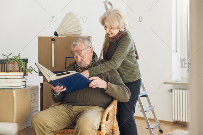 Senior couple looking at photo album surrounded by cardboard boxes in an empty room