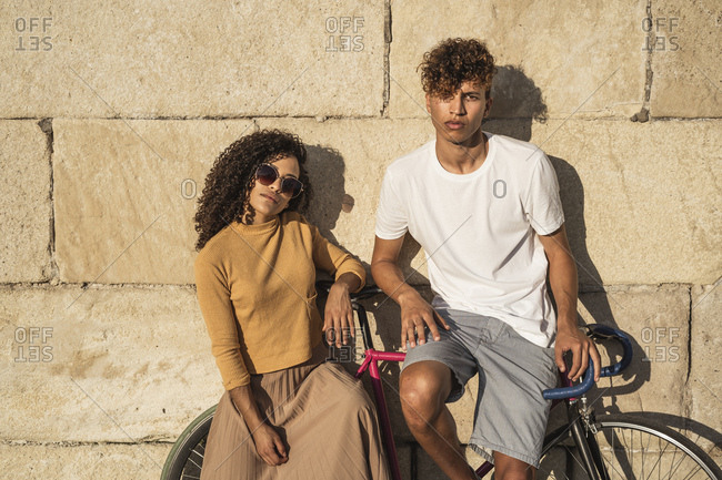Young couple with bicycle- leaning on stone wall- looking cool