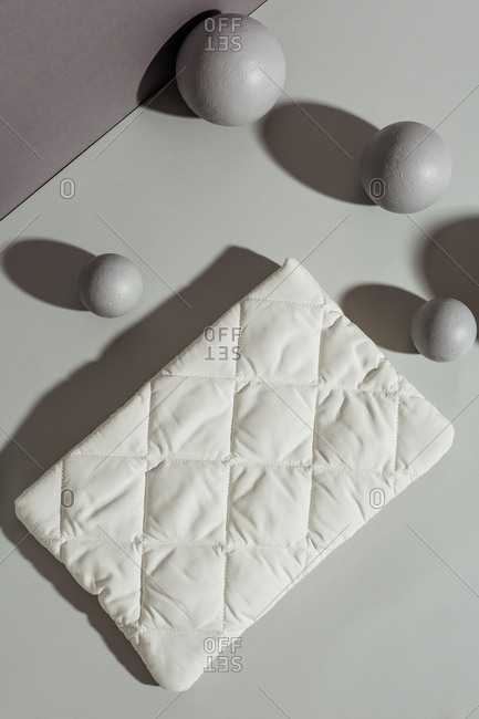 Overhead view of a quilted white pocketbook against grey rectangles and spheres