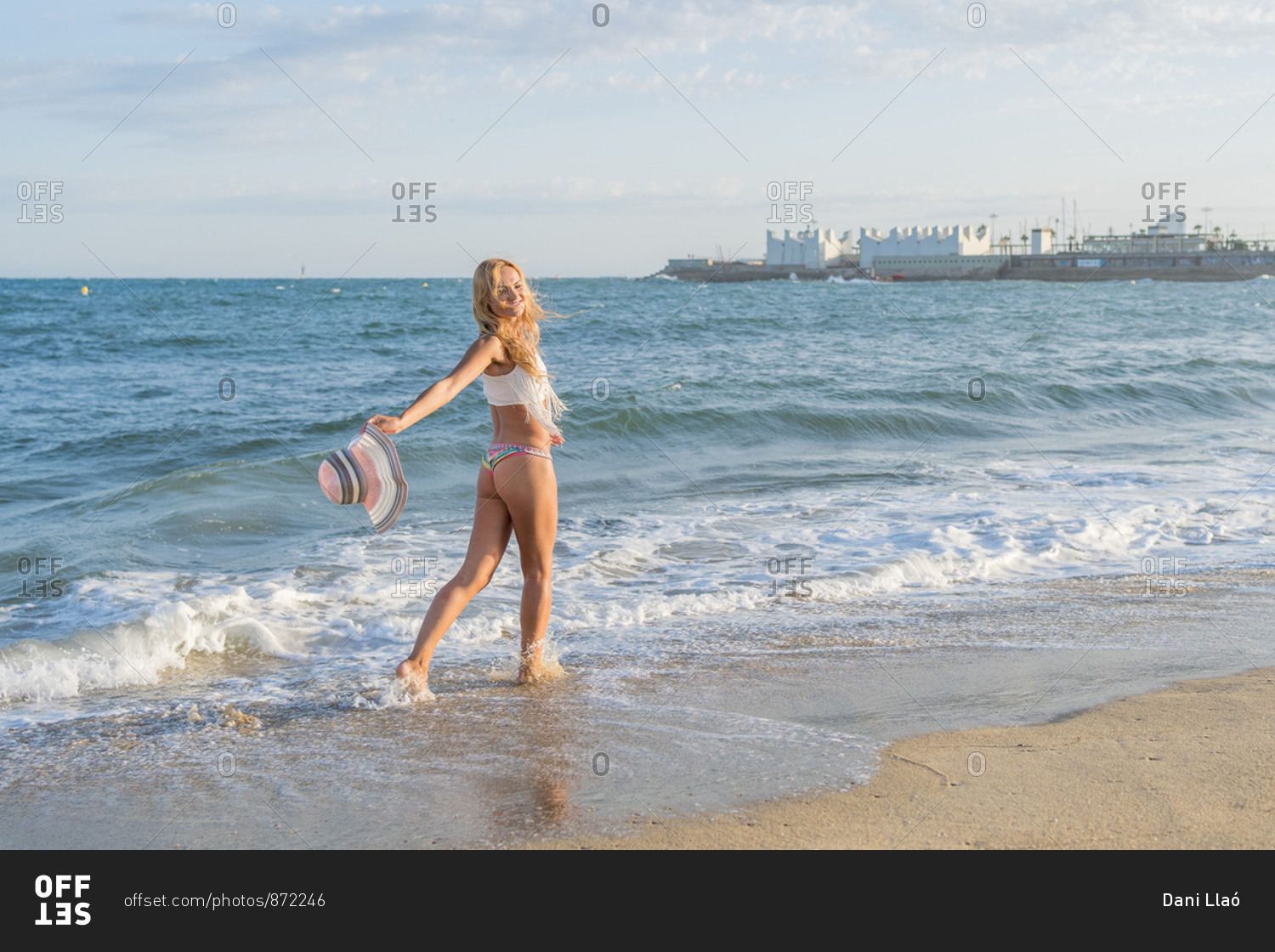 Russian woman smiling as she waves her hat on the shore of the beach