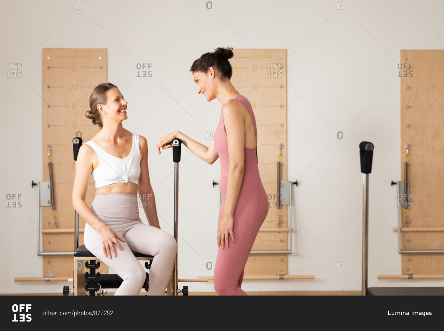 Two pretty smiling sportswomen chatting at pilates studio.