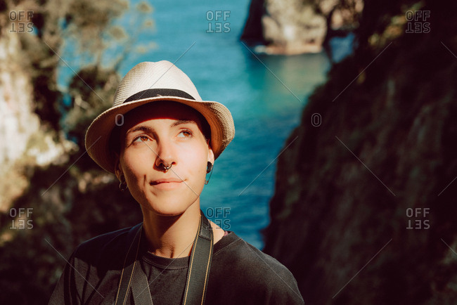 Young woman in hat standing with camera hanging on neck and enjoying picturesque view of sea and rocks in Ribadedeva Asturias Spain