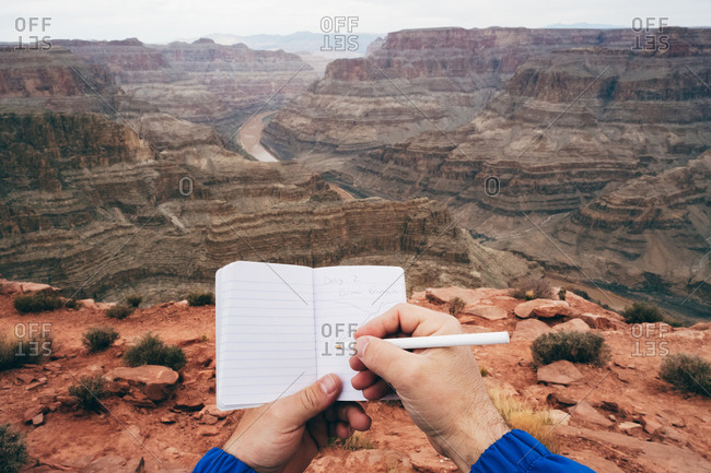 Crop man making notes in diary while having rest at edge of cliff in canyon in USA