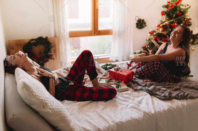 Two beautiful friends laughing in bed at home near Christmas tree in cozy interior. Interior with Christmas decorations.