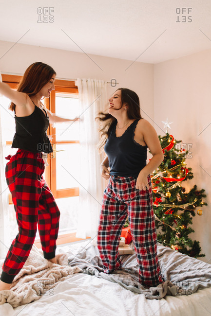 Two beautiful friends jumping and laughing in bed at home near Christmas tree in cozy interior. Interior with Christmas decorations.