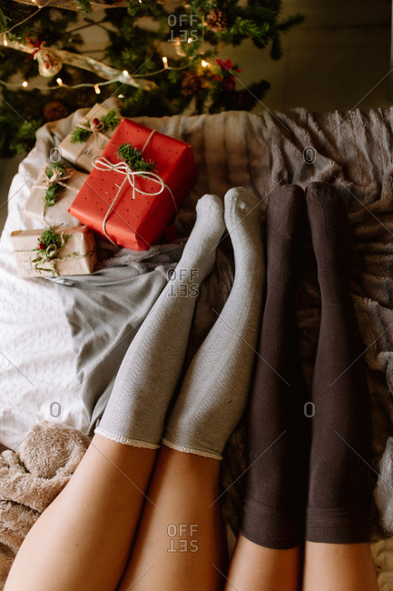 Two friends with knee high socks in winter holidays at home near Christmas tree in cozy interior with Christmas presents.