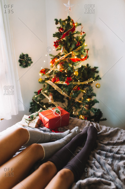 Two women friends with knee high socks in winter holidays at home near Christmas tree and presents in cozy interior.