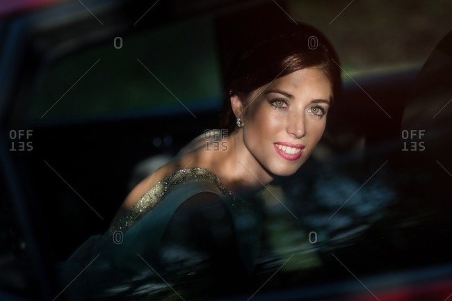Mysterious graceful bride in back seat of car looking out window with thoughtful smile in contrast light