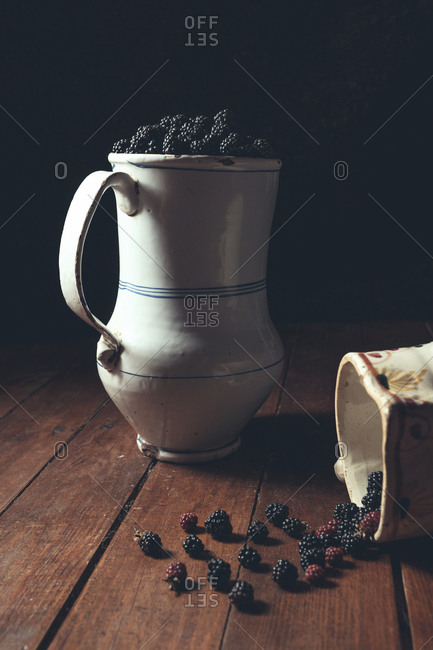 Ripe tasty appetizing blackberries on wooden table and in white decanter in shadow