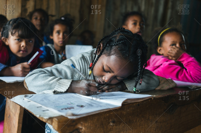 Madagascar - JULY 6, 2019: Attentive African children listening and writing in notebooks while sitting at desks in rural school