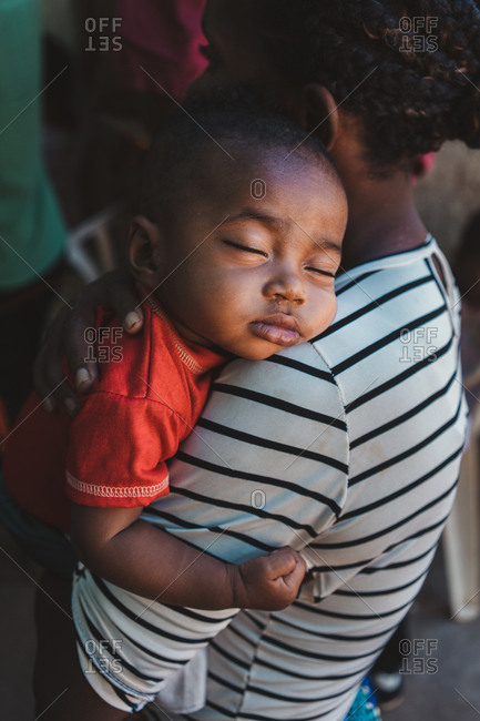 Madagascar - JULY 6, 2019: Side view of casual African woman comforting dreaming peaceful child while standing