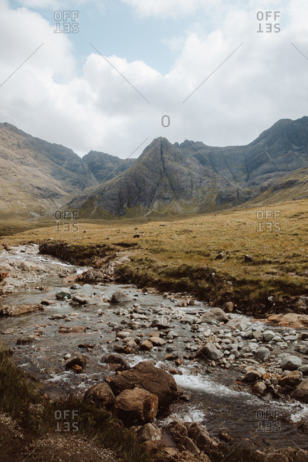 Low angle of clear water with stones in Fairy Pool surrounded by whimsical rocks under cloudy sky