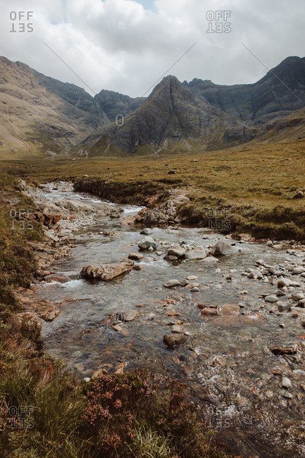 Low angle of clear water with stones in Fairy Pool surrounded by whimsical rocks under cloudy sky