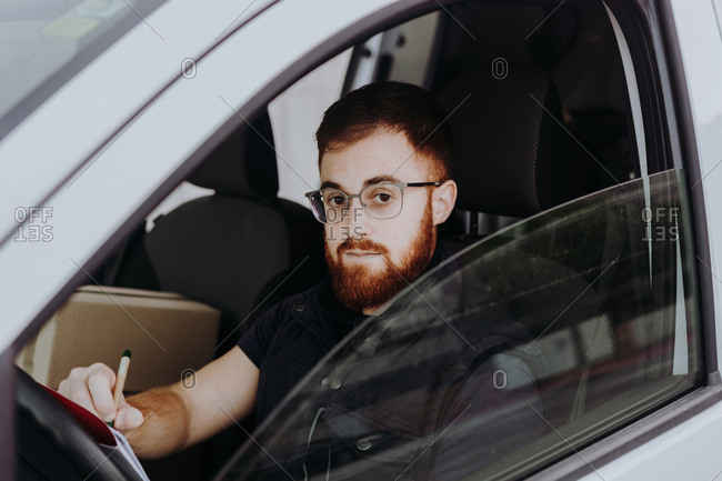 Side view of attentive thoughtful adult man focusing and checking documents while sitting behind steering wheel in car cabin during daytime on blurred background