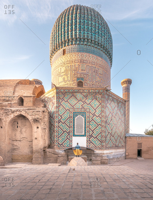 Back view of anonymous woman standing outside Gur-e Amir mausoleum with beautiful ornaments and dome on sunny day in Samarkand, Uzbekistan