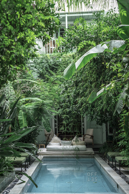 October 22, 2018: Swimming pool and couch located amidst green exotic plants outside hotel building in Marrakesh, Morocco