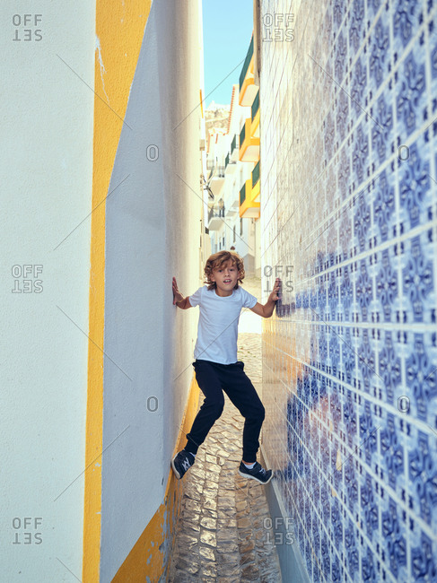 Playful boy scrambling on decorative wall on narrow alley on street in Portugal