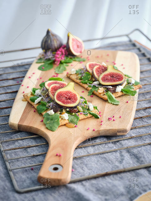 Homemade tasty colorful open sandwiches with slices of fig and pieces of cheese on crisp rye bread among aromatic green leaves of rocket salad and pink flowers