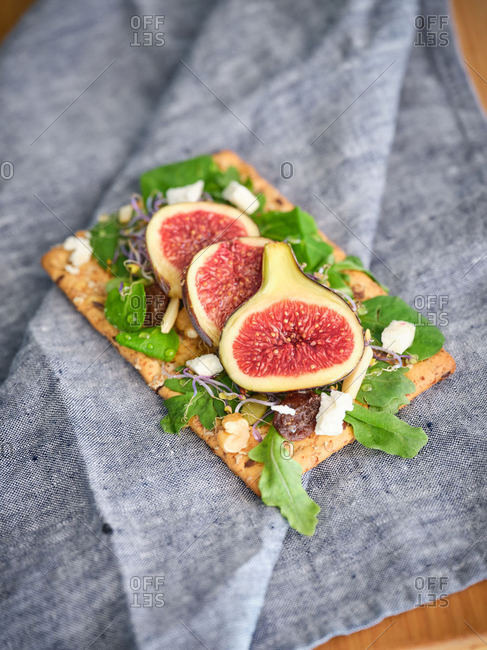 Homemade delicious colorful open sandwich with slices of fig and pieces of cheese on crisp rye bread among aromatic green leaves of rocket salad