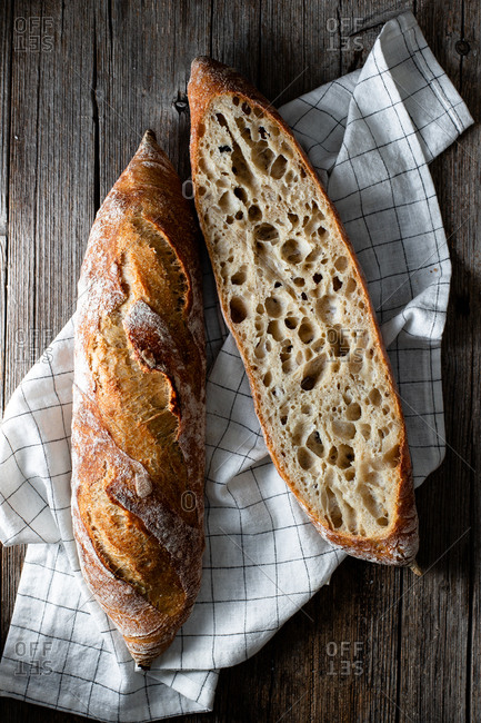 From above whole and halved appetizing baguettes arranged on white towel against rustic wooden background