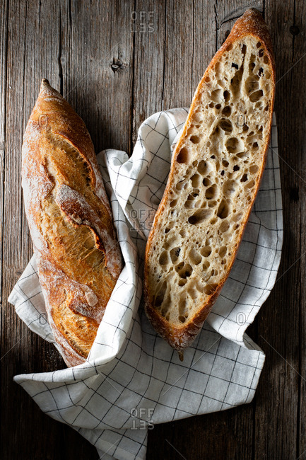 From above whole and halved appetizing baguettes arranged on white towel against rustic wooden background