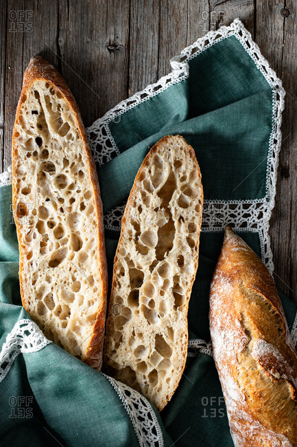 From above whole and halved appetizing baguettes arranged on white towel against rustic wooden background