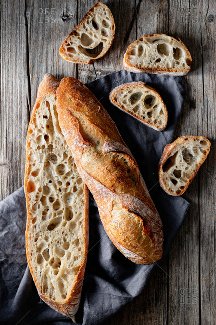 From above whole and halved appetizing baguettes arranged on white towel against rustic wooden background