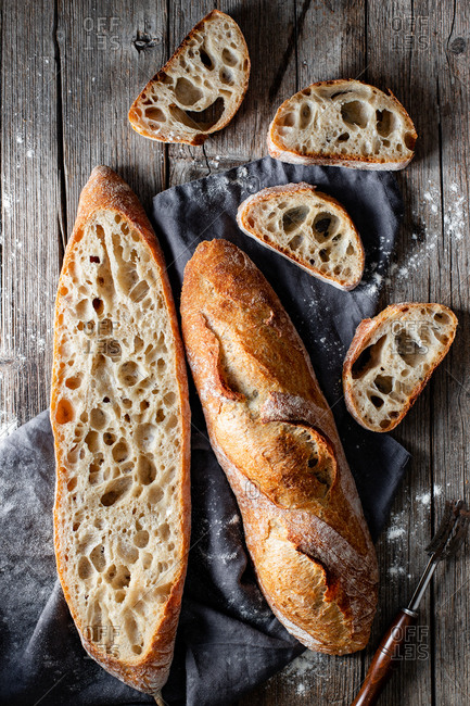 From above whole and halved appetizing baguettes arranged on white towel against rustic wooden background