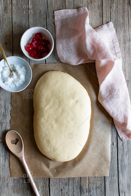 From above dough on baking paper and ingredients prepared for cooking Spanish pie called coca San Juan on wooden table