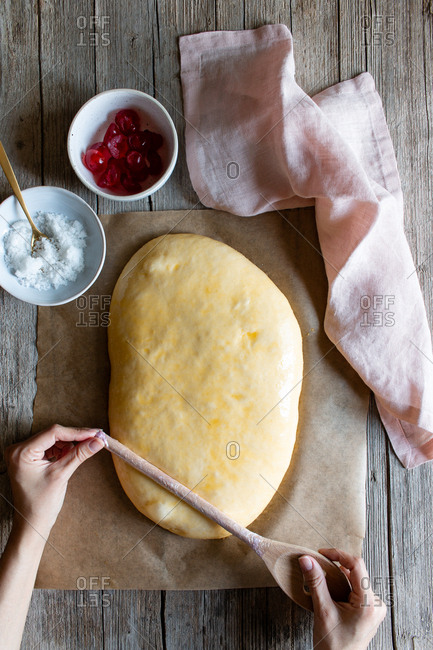 Overhead crop baker making lines with wooden spoon on dough prepared for cooking traditional pastry coca San Juan at home