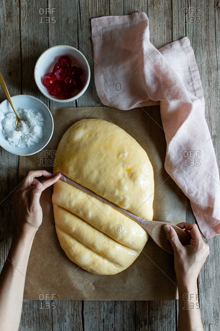 Overhead crop baker making lines with wooden spoon on dough prepared for cooking traditional pastry coca San Juan at home