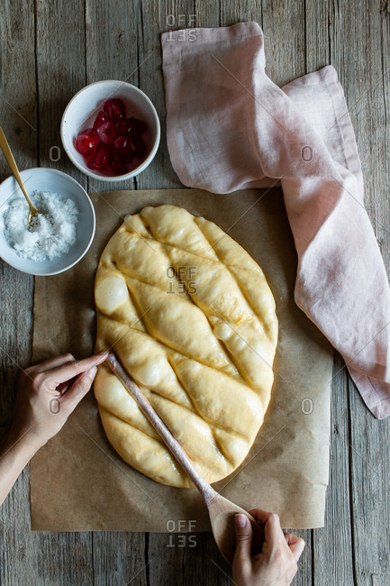 Overhead crop baker making lines with wooden spoon on dough prepared for cooking traditional pastry coca San Juan at home