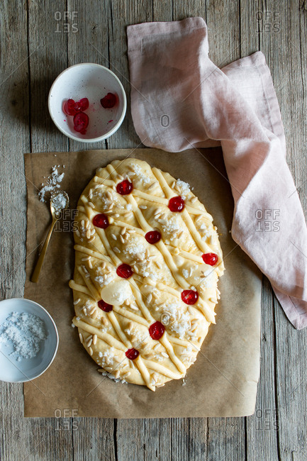 Top view of fresh Coca de San Juan pastry with seeds and open recipe book placed on timber table near towel and knife in rustic kitchen