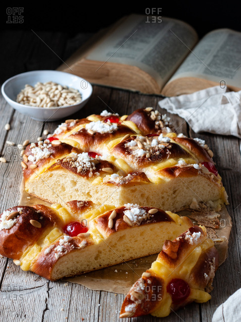 fresh Coca de San Juan pastry with seeds and open recipe book placed on timber table near towel and knife in rustic kitchen