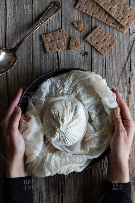 Overhead crunchy crackers and spoon placed near plate with ball of fresh labneh cheese on lumber table