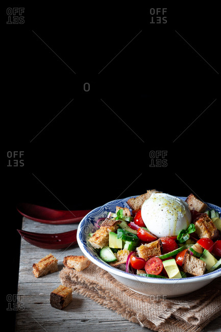 Bowl with yummy panzanella salad placed on cloth on wooden table against black background
