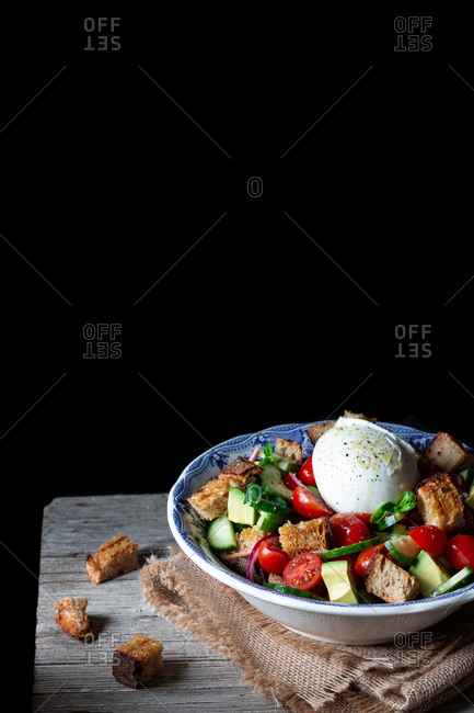 Bowl with yummy panzanella salad placed on cloth on wooden table against black background