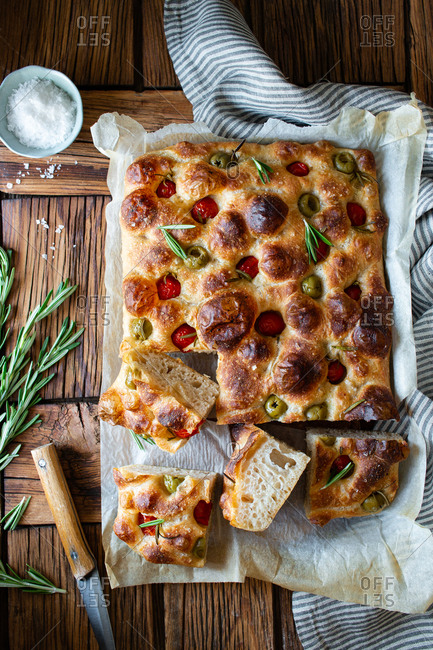 Overhead potato focaccia with fresh rosemary placed near bowl with salt and striped napkin on wooden table