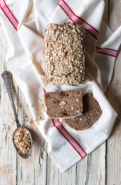 From above loaf of tasty ryecorn bread placed on cloth napkin near spoon of grain on wooden background