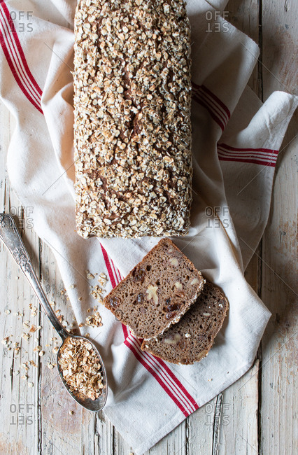 From above loaf of tasty ryecorn bread placed on cloth napkin near spoon of grain on wooden background