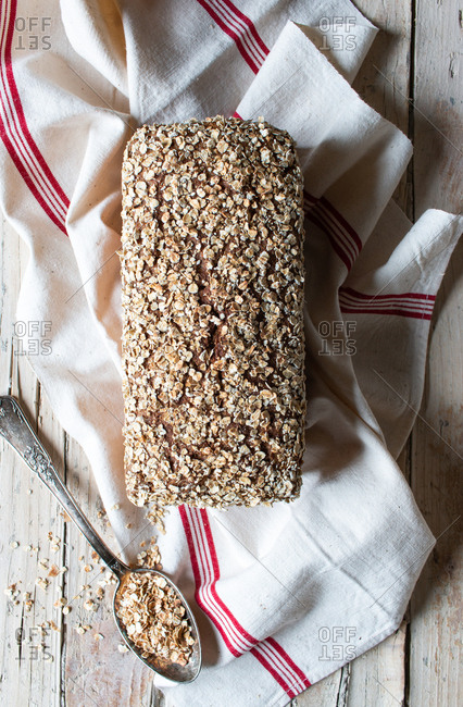 From above loaf of tasty ryecorn bread placed on cloth napkin near spoon of grain on wooden background