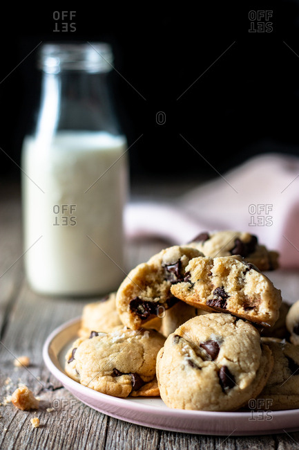 Plate of tasty vegan cookies with chocolate chips placed on lumber table near blurred milk and cloth against black background