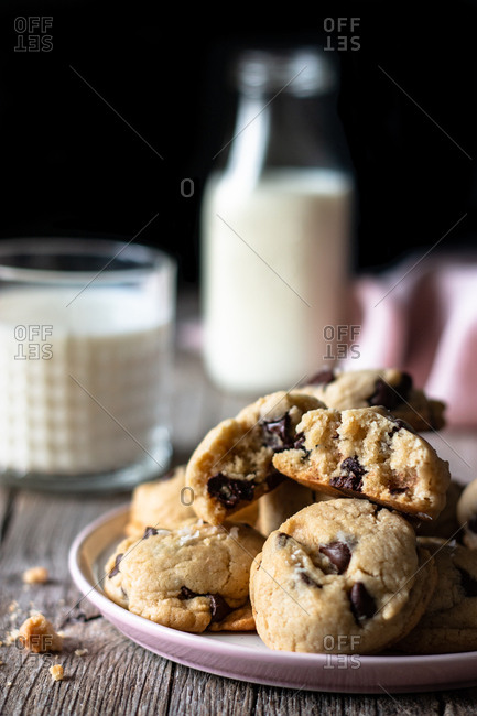 Plate of tasty vegan cookies with chocolate chips placed on lumber table near blurred milk and cloth against black background