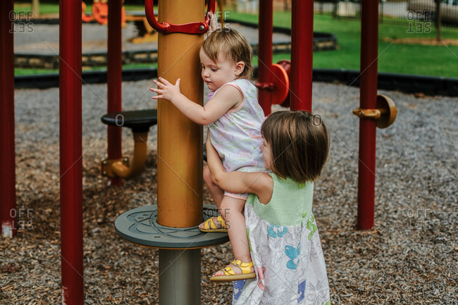 A big sister helps a little sister down from a playground structure